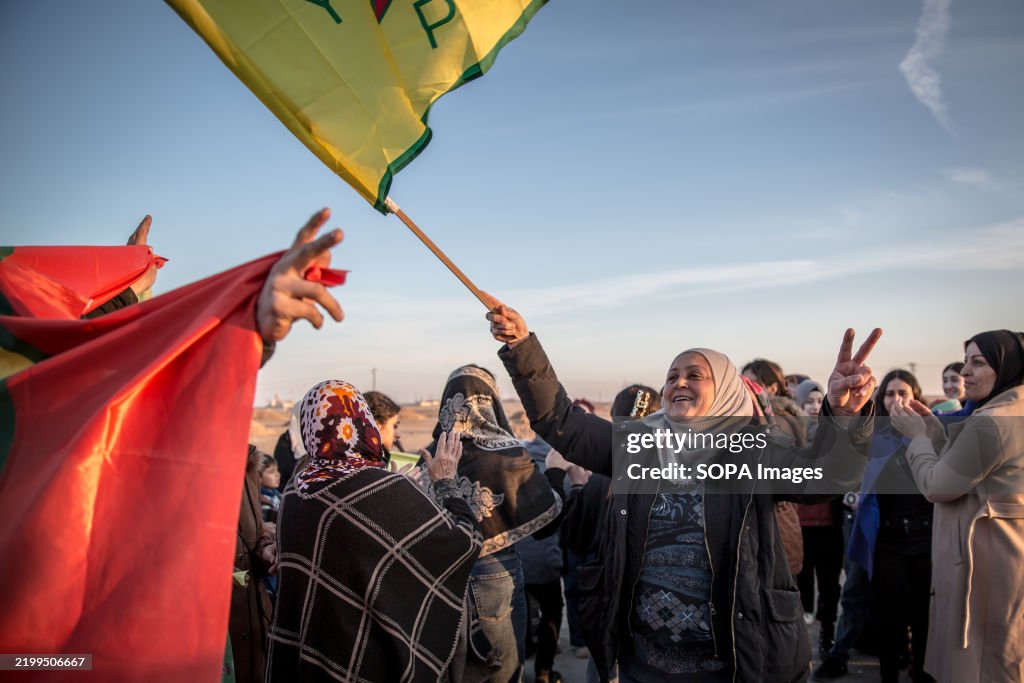 A woman waves a YPG flag as friends and family members...