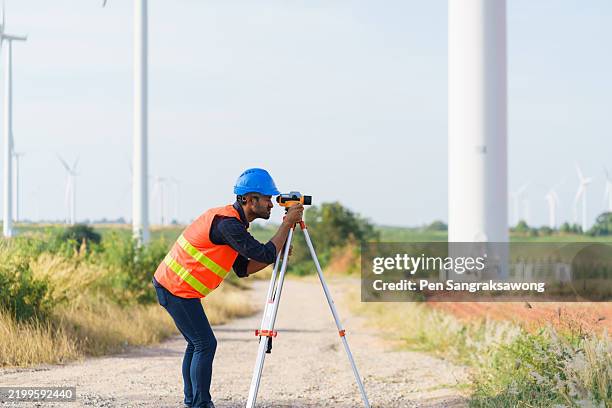 a young engineer is looking through a survey camera to level the area for road construction in a wind power generating area. - tacheometer stock pictures, royalty-free photos & images