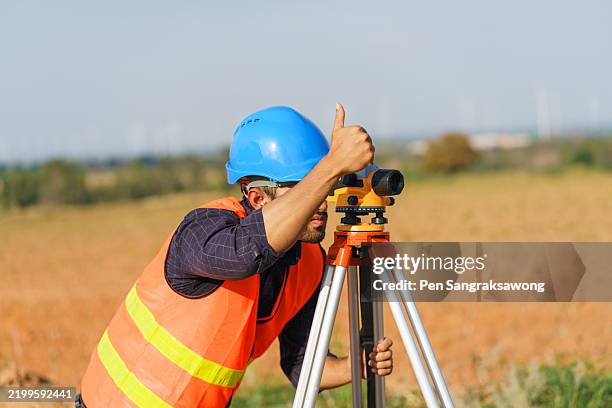 a young engineer is looking through a survey camera to level the area for road construction in a wind power generating area. - tacheometer stock pictures, royalty-free photos & images