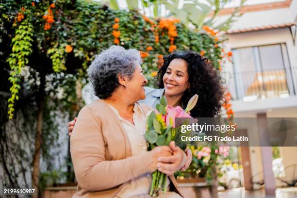 mid adult woman embracing and giving flowers to mother outdoors - mothers day stock pictures, royalty-free photos & images