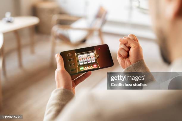 personne célébrant un gain en jouant à un jeu de machine à sous sur smartphone - casino interior photos et images de collection