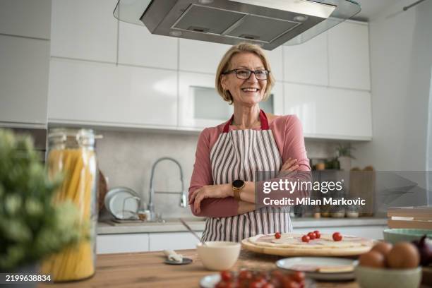 femme d’âge moyen souriant les bras croisés et faisant de la pizza dans la cuisine - tablier photos et images de collection