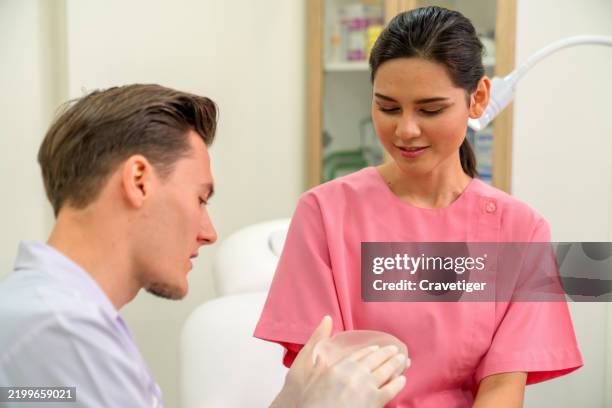 docotr explain to patient woman is choosing breast implants in beauty treatment clinic. - beauty therapist in uniform stock pictures, royalty-free photos & images