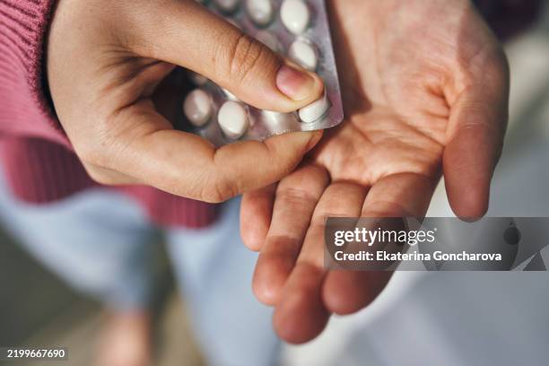 close-up of a hand holding pills and a blister pack - pillen stockfoto's en -beelden