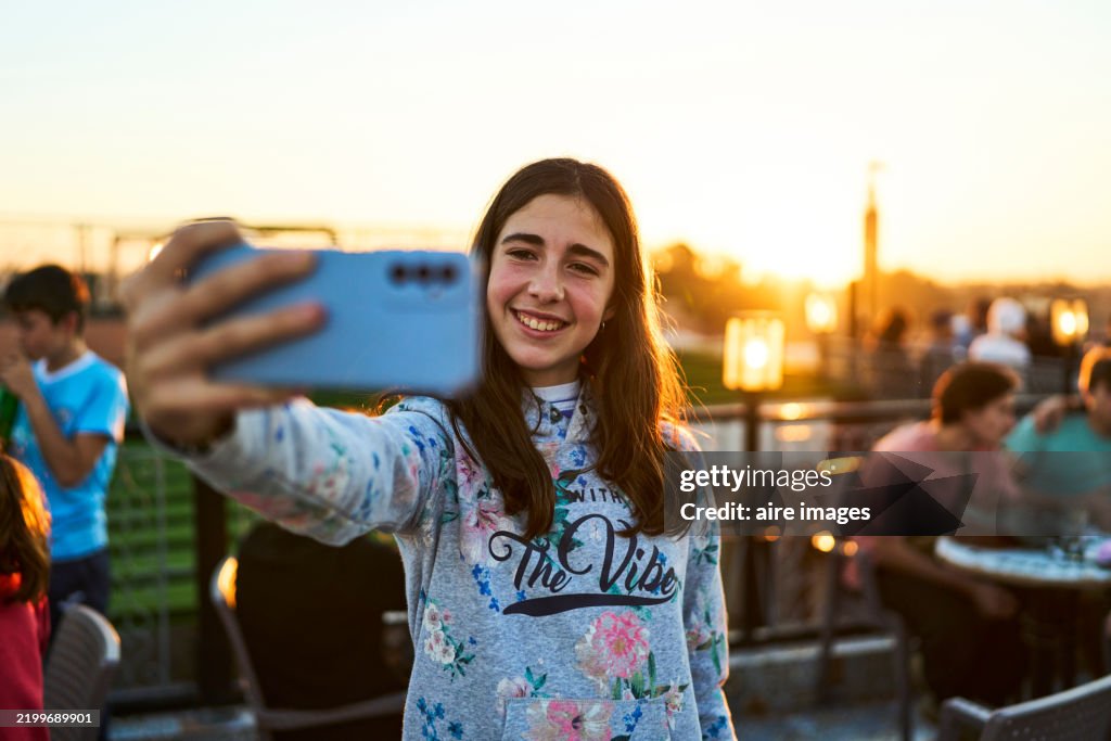 Front view of a beautiful young woman standing taking a selfie during Marrakesh sunset, looking at the camera