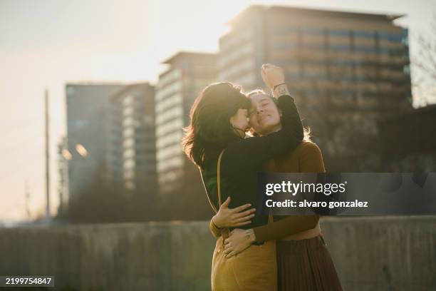 lesbian couple embracing in the city at sunset - lesbica foto e immagini stock