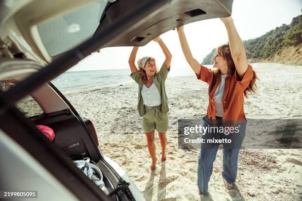two cheerful female friends closing car trunk at the beach - car trunk closed stock pictures, royalty-free photos & images