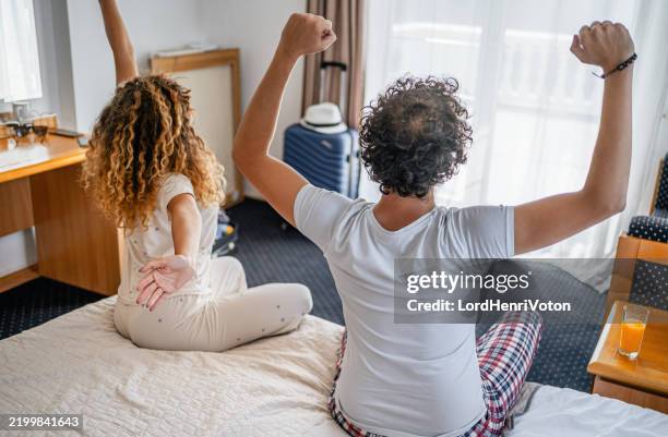 couple stretching their arms after sleep in hotel room - heteroseksueel koppel stockfoto's en -beelden