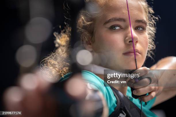 focused teenage caucasian female archer in studio shot - vaardigheid stockfoto's en -beelden