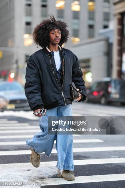 Guest wears a headband, a black bomber jacket, blue flared wide-leg denim pants / jeans, suede shoes, outside Diotima, during New York Fashion Week,...
