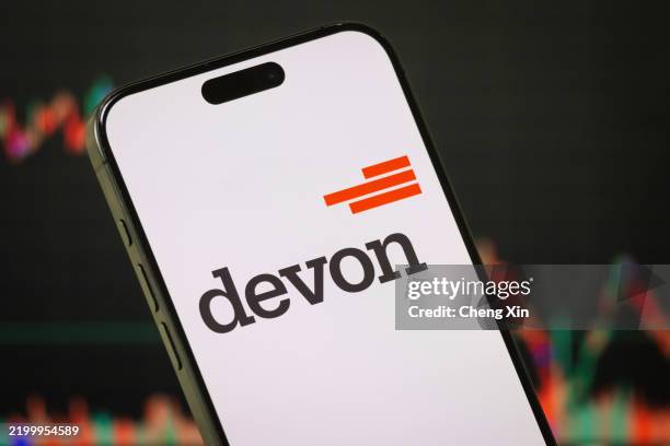 In this photo illustration - The Devon Energy logo is displayed on a smartphone screen in front of a stock chart showcasing Devon Energy's financial...