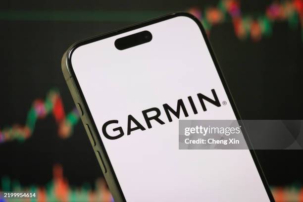 In this photo illustration - The Garmin logo is displayed on a smartphone screen in front of a stock chart showcasing Garmin's financial performance,...