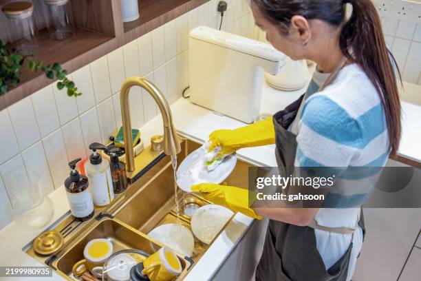 domestic duties, woman washing dishes at kitchen sink - housewife stock pictures, royalty-free photos & images