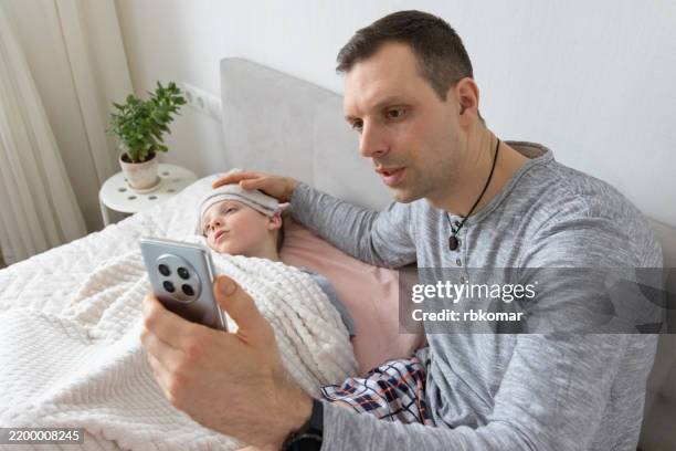 medical consultation happens through smartphone screen. devoted parent monitors resting child during virtual doctor visit - symptom stock-fotos und bilder