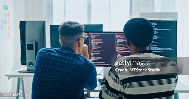 two male software developers meeting on multiple computer screens displaying programming code, collaborating on project in office. artificial intelligence and programming. - web designer imagens e fotografias de stock