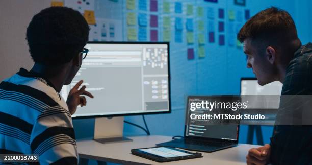 group of it professionals collaborating on network security and data analysis using digital tablet and laptop in office at night. software developer, artificial intelligence and programming. - software development stock pictures, royalty-free photos & images