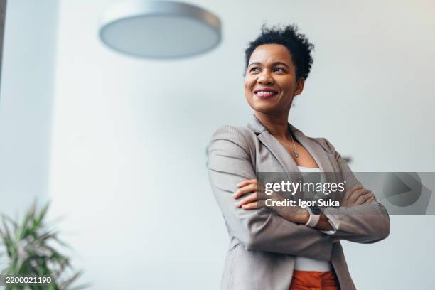 mujer de negocios segura de sí misma sonriendo y mirando hacia otro lado en una oficina moderna - recto vestimenta fotografías e imágenes de stock