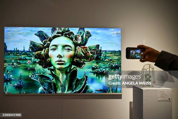 Person takes a picture of AI artwork created by Vanessa Rosa called 'Little Martians & Abraham' at a press preview for 'Augmented Intelligence' at...