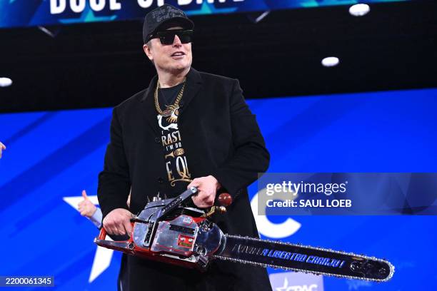 Elon Musk holds a chainsaw reading "Long live freedom, damn it" during the annual Conservative Political Action Conference at the Gaylord National...