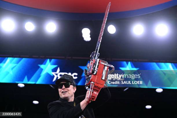 Elon Musk holds a chainsaw reading "Long live freedom, damn it" during the annual Conservative Political Action Conference at the Gaylord National...