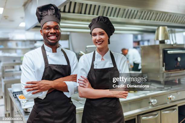 two smiling chefs posing with arms crossed in a restaurant kitchen - catering building stock pictures, royalty-free photos & images