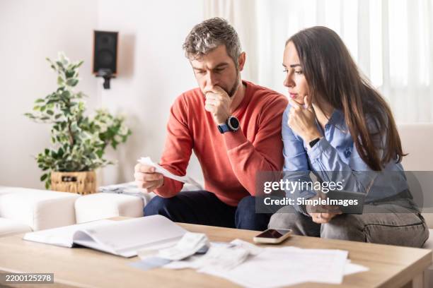 a young couple checks their bank statements and mortgage contracts to determine their financial ability - bad news stock pictures, royalty-free photos & images