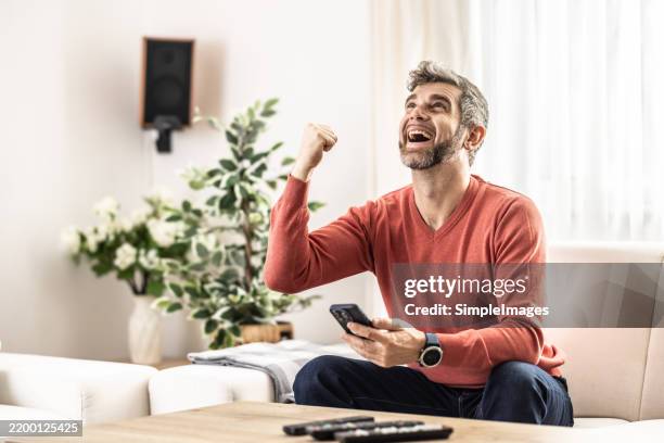a young man is happy about the good news that came to him on his smartphone. - lotterie stock-fotos und bilder