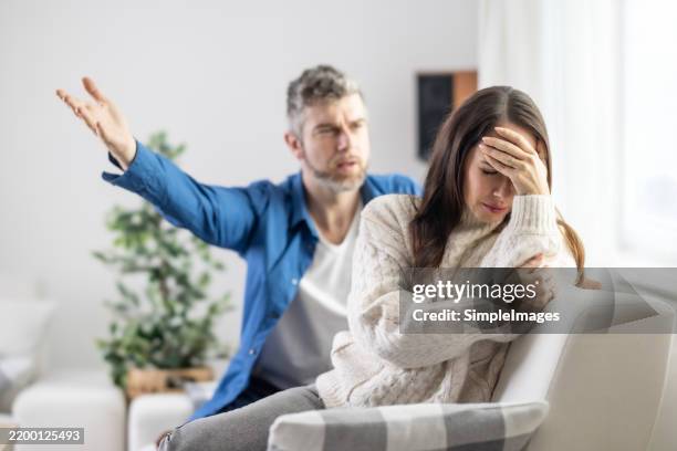 the husband shouts at the partner, who ignores him and holds her head in frustration - se disputer photos et images de collection