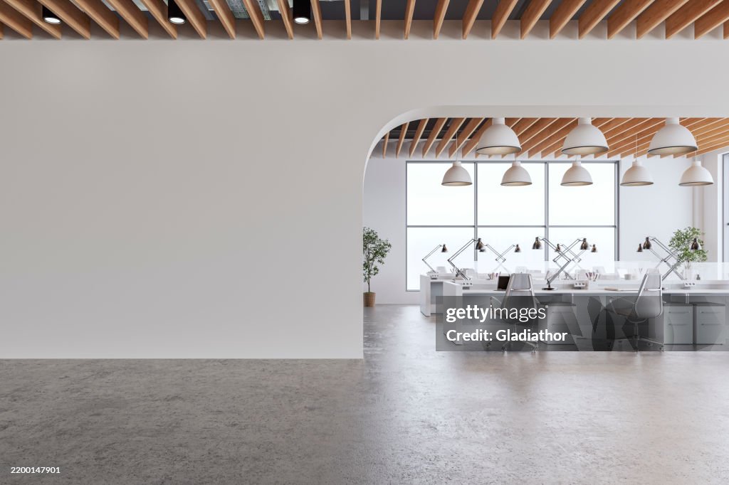 Semi-empty office interior with arched white blank wall and copy space, a wooden slats ceiling, work desks and large windows, on cement floor