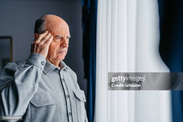 worried senior man looking out the window - neurodegenerative disease stock pictures, royalty-free photos & images