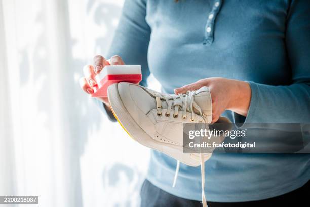 unrecognizable woman rubbing white sneakers with a special cleaning sponge at home - clean white shoes stock pictures, royalty-free photos & images