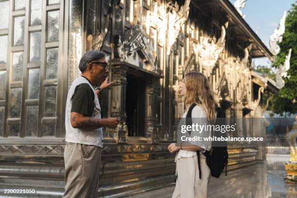 a senior tour guide showing a foreign tourist the buddha statue while explaining symbolism and craftsmanship - critic stock pictures, royalty-free photos & images