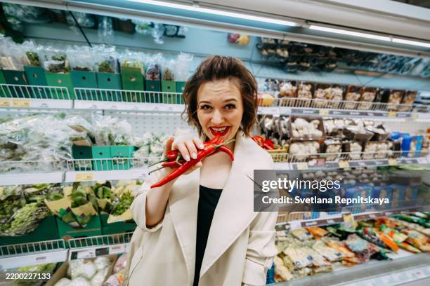 young woman holding chili peppers at the supermarket - red chili pepper stock pictures, royalty-free photos & images