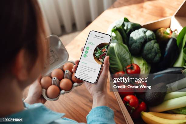 over the shoulder view of young woman looking at healthy recipe on smartphone over meal kits delivery - convenience stock pictures, royalty-free photos & images