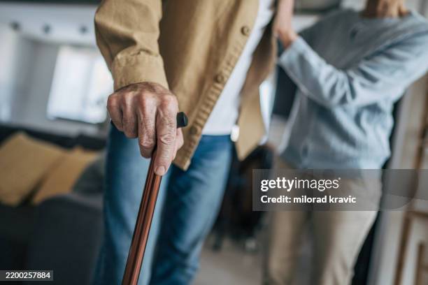 senior man holding walking cane while nurse assists him at home - walking cane stock pictures, royalty-free photos & images