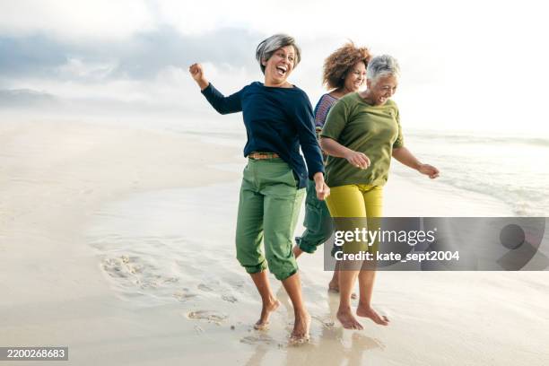 women enjoying retirement, friendship, and the tranquility of the beach - actieve ouderen stockfoto's en -beelden