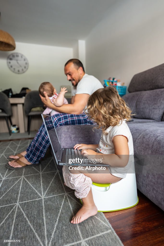 Little girl using laptop while potty training and father playing with baby