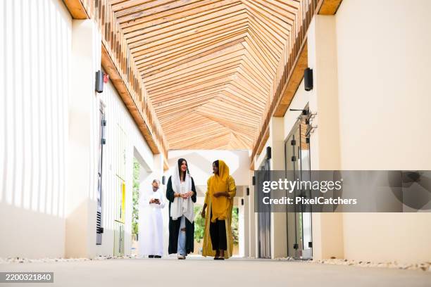 wide shot two young women walking down outdoor corridor with designer wooden roof - arab fashion designer stock pictures, royalty-free photos & images
