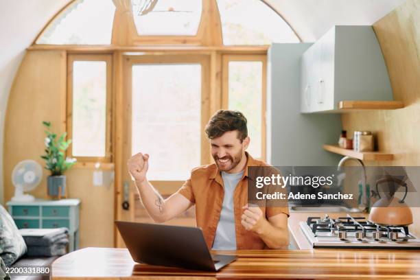 man, laptop and winner with cheers in kitchen, home and fist pump for success, profit or goals. person, smile and celebration with online giveaway, lotto or excited for financial freedom at apartment - giveaway stock pictures, royalty-free photos & images