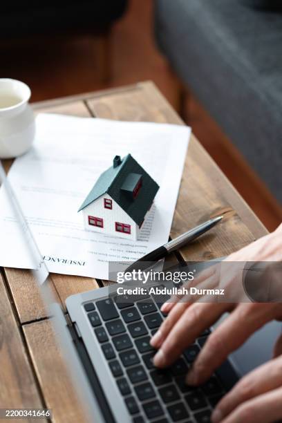 insurance agent typing on laptop with house model and insurance policy - seguro de habitação imagens e fotografias de stock