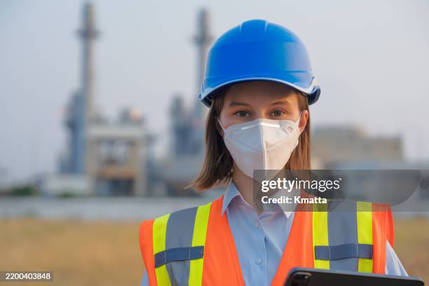 close-up of a female engineer wearing protective face mask with power plant background. this concept reflects the collective efforts to prioritize health and safety during a time when air pollution is on the rise. - respiratory protection construction stock pictures, royalty-free photos & images