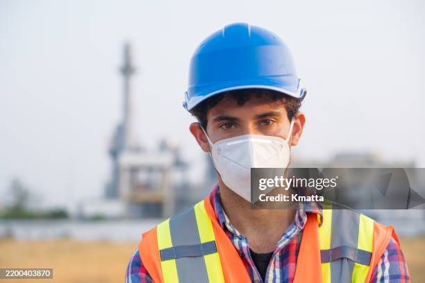 close-up of a male engineer wearing protective face mask with power plant background. this concept reflects the collective efforts to prioritize health and safety during a time when air pollution is on the rise. - respiratory protection construction stock pictures, royalty-free photos & images
