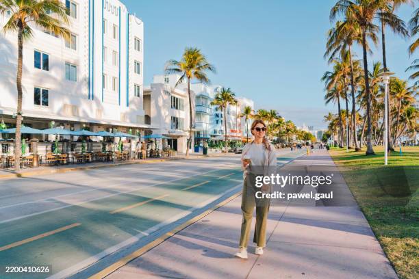 woman holding coffee walks along ocean drive in miami beach, art deco historic district florida usa - miami bildbanksfoton och bilder