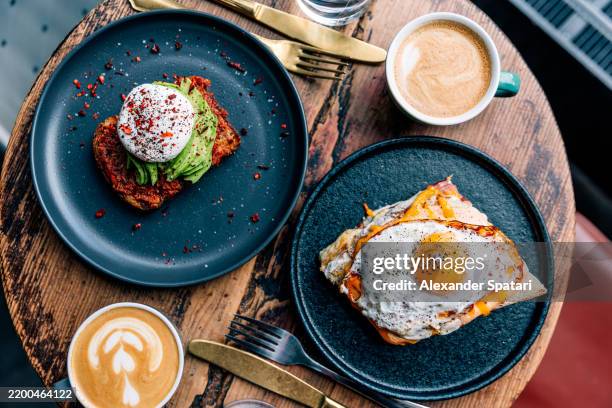 avocado and poached egg on toasted bread and croque madame with fried egg served for breakfast at a restaurant, directly above view - croque monsieur stockfoto's en -beelden