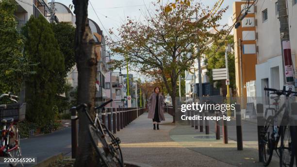 woman walking in a quiet urban street - dichterbij komen stockfoto's en -beelden