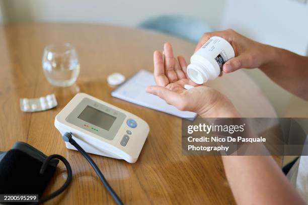 man taking medication with a blood pressure monitor on the table - bluthochdruck stock-fotos und bilder