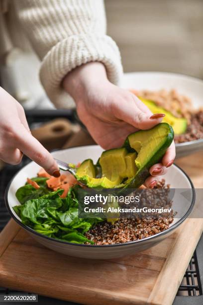 female adding avocado slices to salad bowl for extra healthy fats - positioning stock pictures, royalty-free photos & images