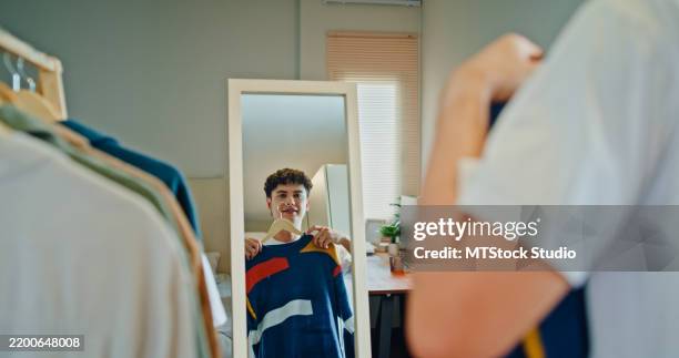 hombre joven eligiendo con confianza un atuendo, parado frente al espejo en el dormitorio de su casa. estilo de vida saludable en la rutina matutina. - un solo hombre fotografías e imágenes de stock