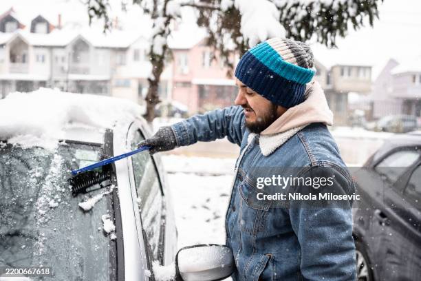 mann reinigt schnee vom auto im winter urbane nachbarschaftsszene - eiskratzer stock-fotos und bilder