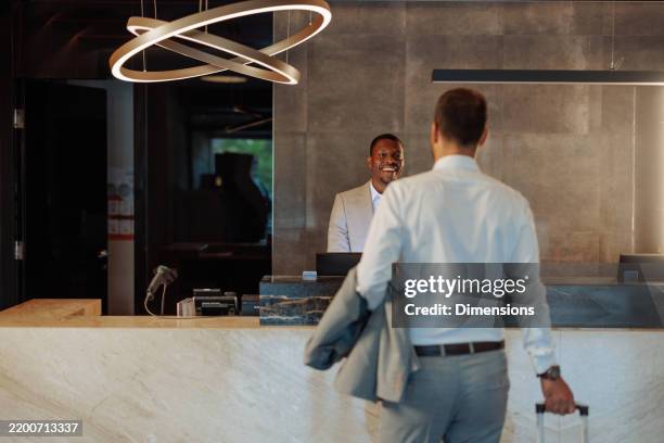businessman arriving at hotel checking in at reception - hotel receptionist stock pictures, royalty-free photos & images